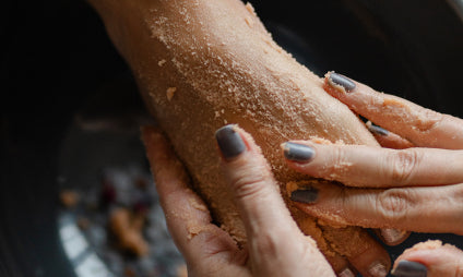 Hands applying a scrub to a foot, with a focus on the gritty texture.