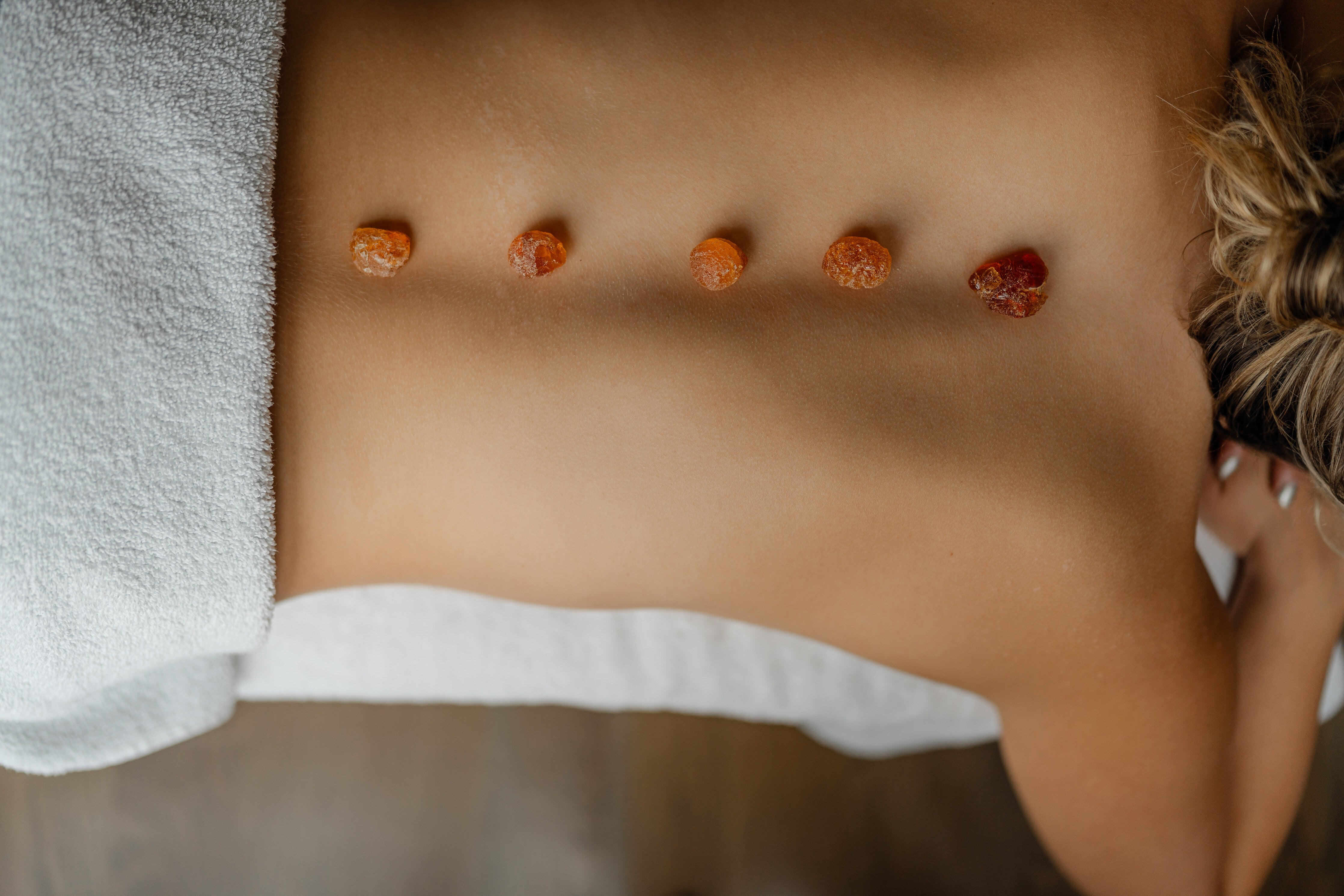 A woman receiving a soothing back massage with warm orange stones, promoting relaxation and wellness.